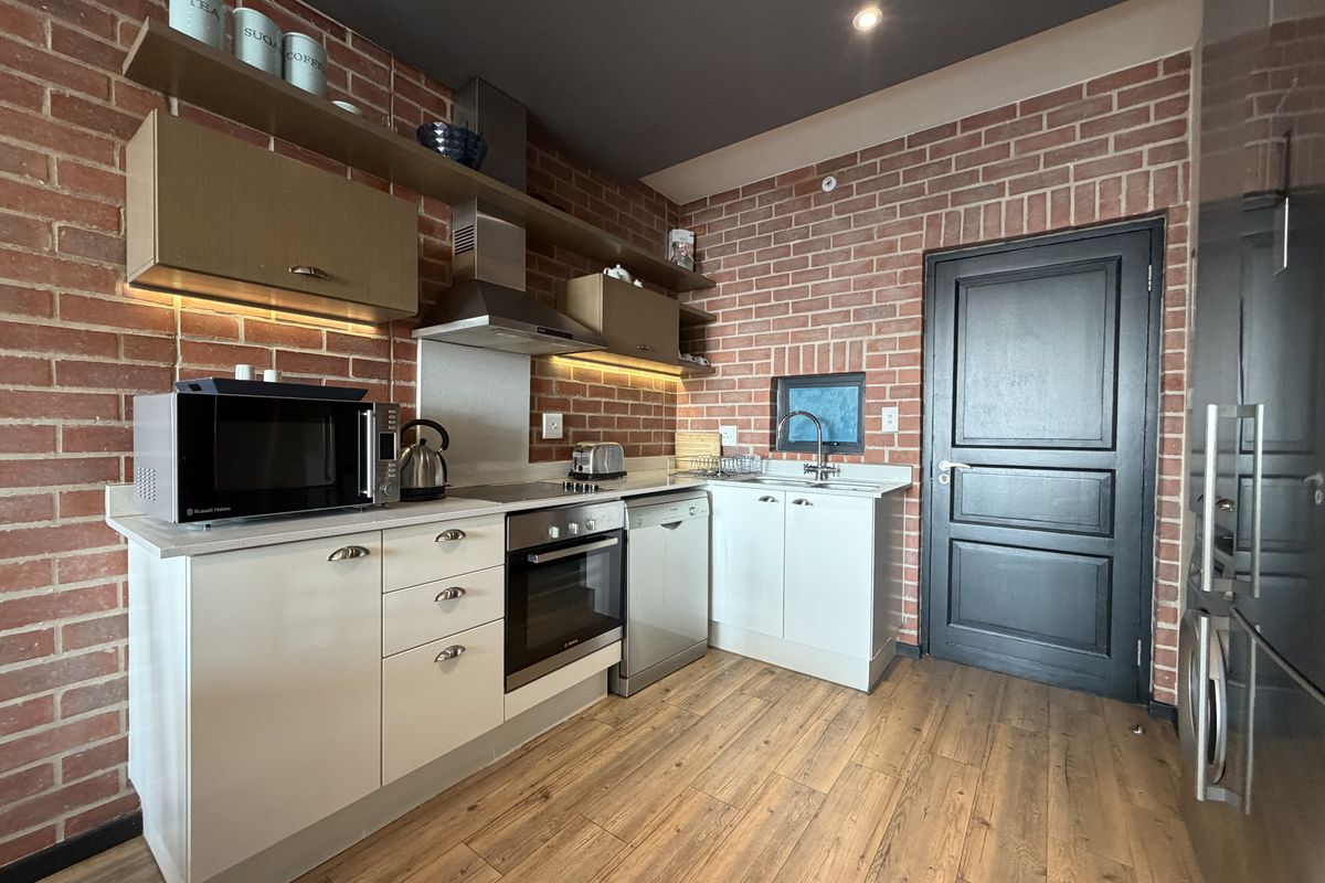 Modern kitchen featuring exposed brick walls, sleek white cabinetry, integrated appliances, and warm laminate flooring, creating a stylish and functional culinary space.