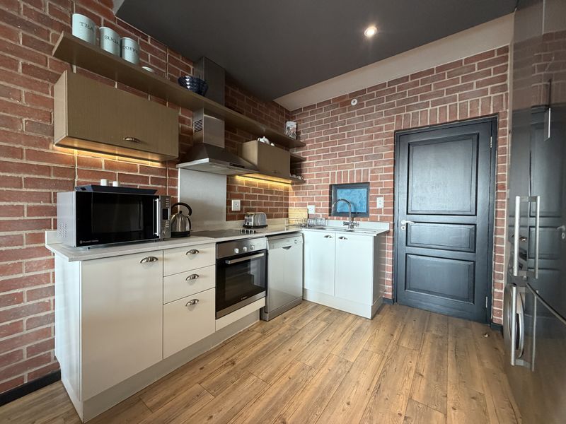 Modern kitchen featuring exposed brick walls, sleek white cabinetry, integrated appliances, and warm laminate flooring, creating a stylish and functional culinary space.