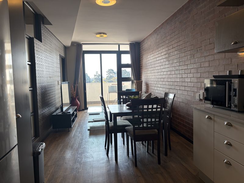 Open-plan living and dining area featuring exposed brickwork, laminate flooring, and direct access to a balcony through sliding glass doors.