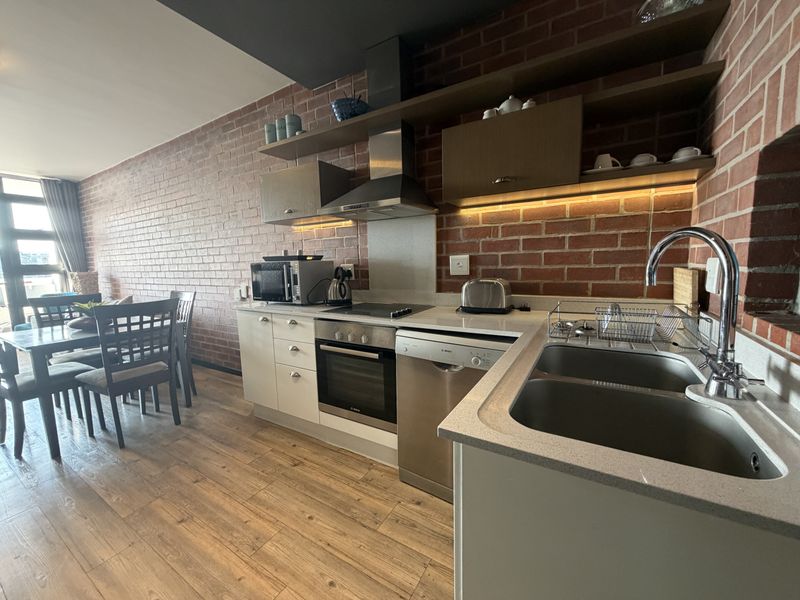 Modern open-plan kitchen featuring exposed brick walls, stone countertops, integrated appliances, and sleek cabinetry, seamlessly flowing into the dining area.