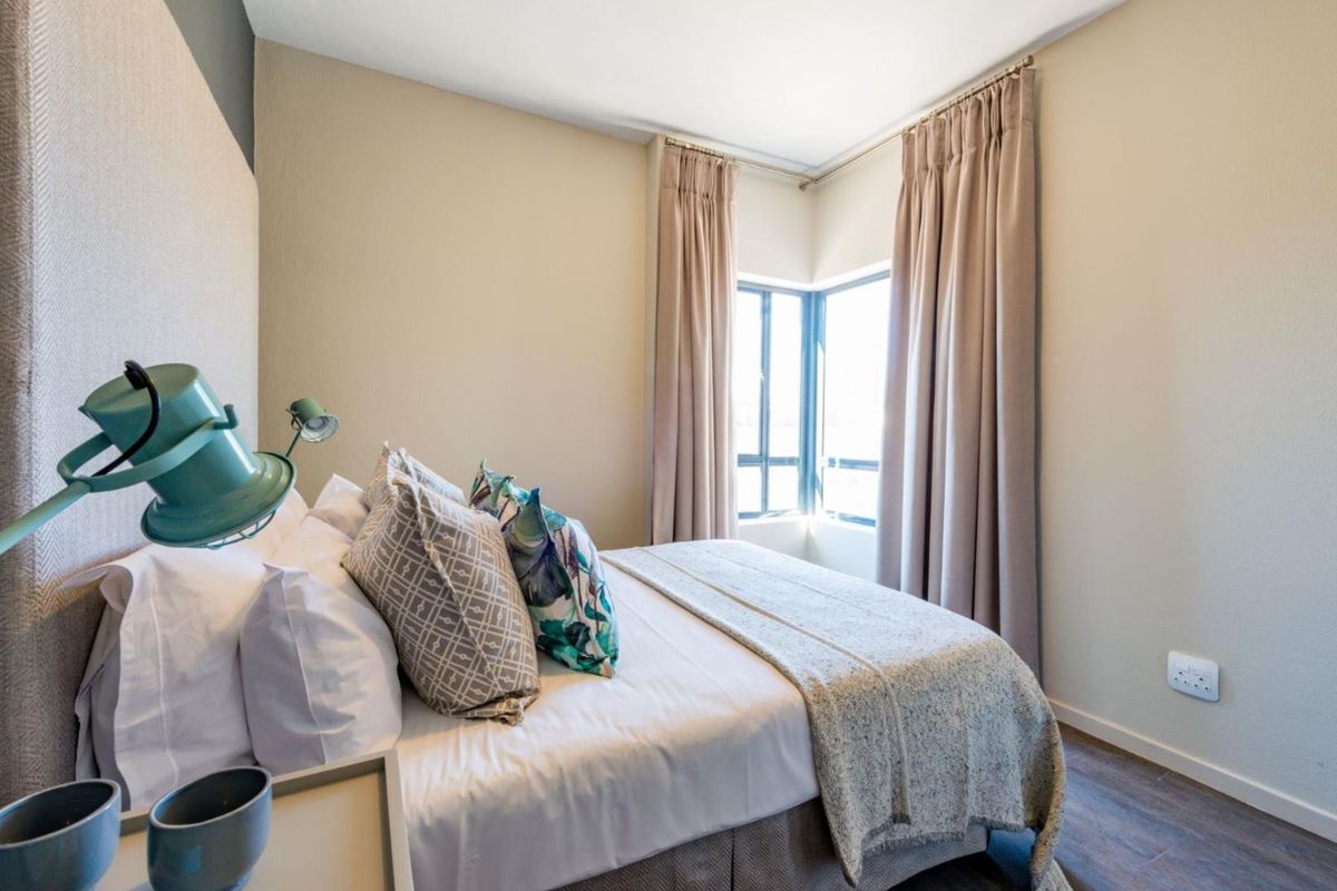 A well-lit bedroom featuring laminate flooring, a corner window with neutral curtains, and a neutral color palette.