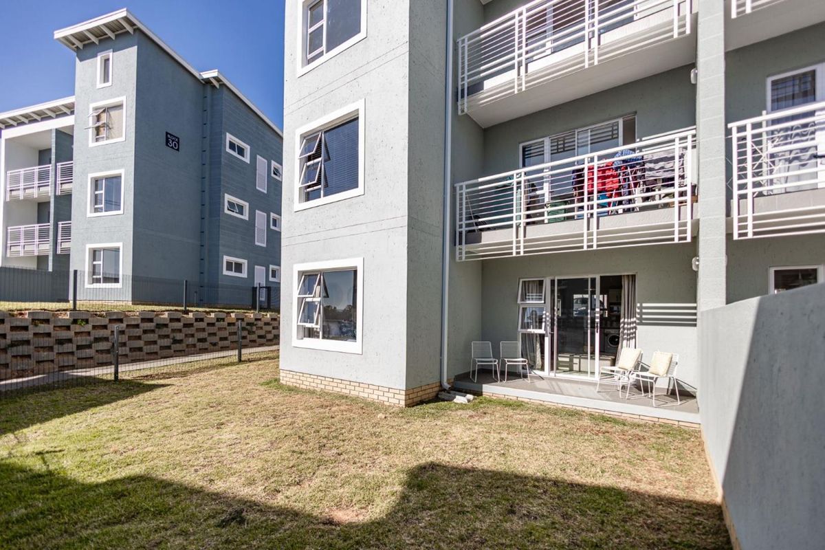 Rear view of the apartment building featuring a ground floor patio, upper-level balconies, and a small private garden area.