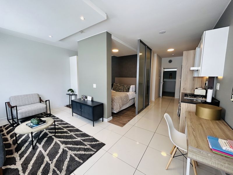 Modern open-plan apartment featuring a combined living area, kitchen with built-in cabinetry, and a partitioned bedroom space with sliding glass doors.