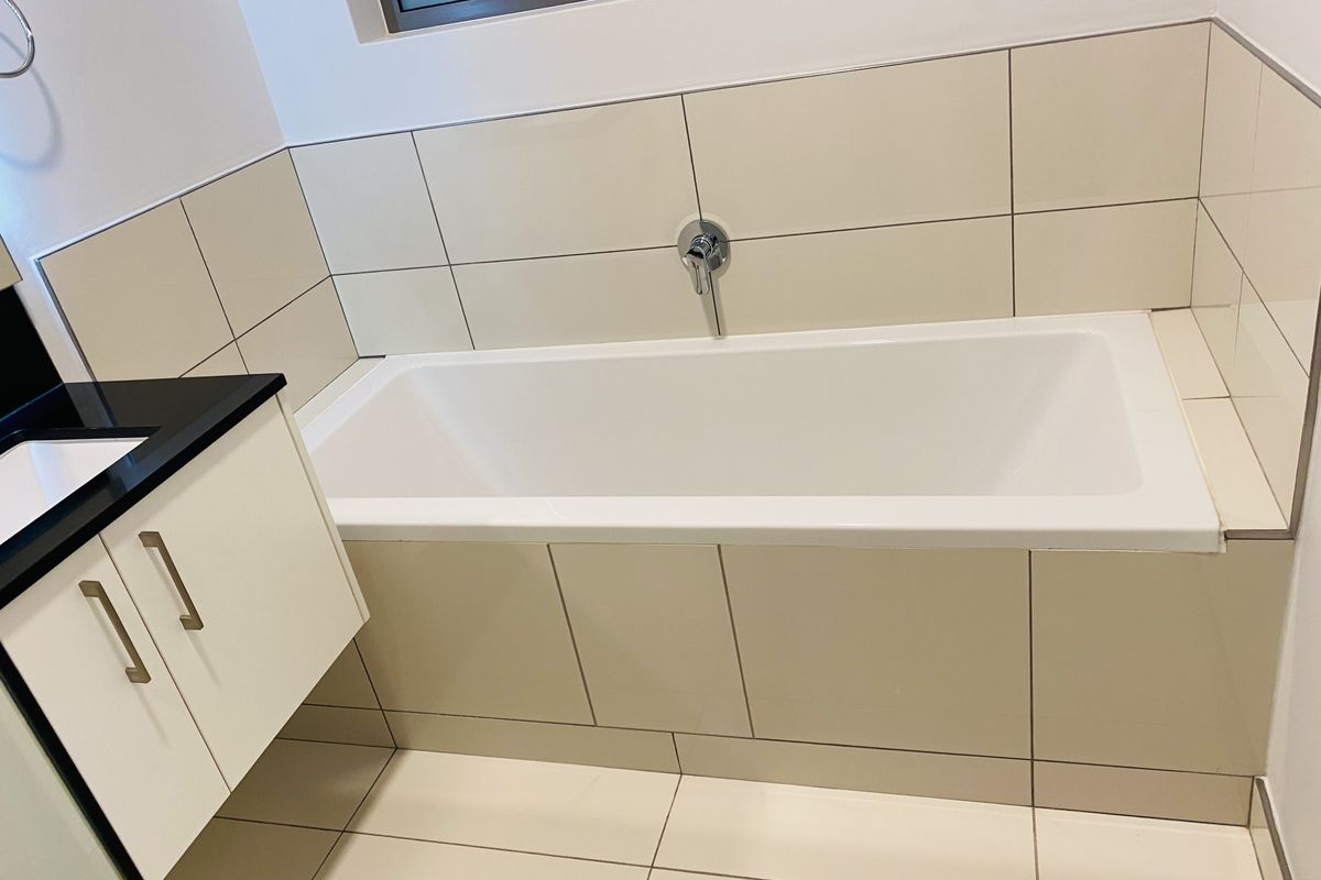 A clean, modern bathroom featuring a built-in bathtub with wall-mounted fixtures and a vanity cabinet with a stone countertop.