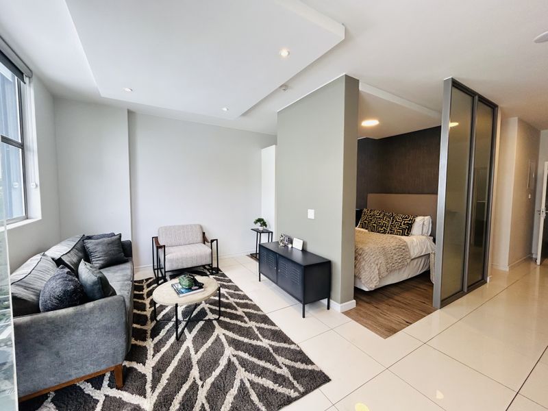 Modern open-plan apartment featuring a living area with tiled floors and a partitioned bedroom space with wood-look flooring and a sliding glass door.