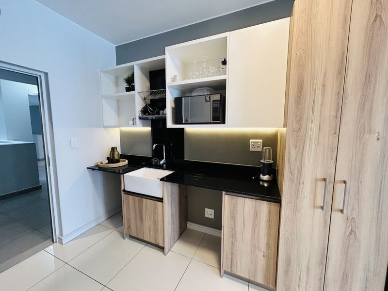 Modern kitchen featuring light wood cabinetry, sleek black countertops, a farmhouse sink, and integrated under-cabinet lighting.