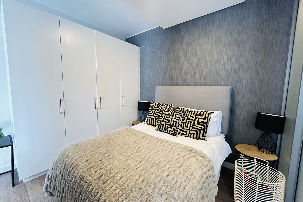 A well-maintained bedroom featuring a large built-in wardrobe, modern laminate flooring, and a stylish textured feature wall.