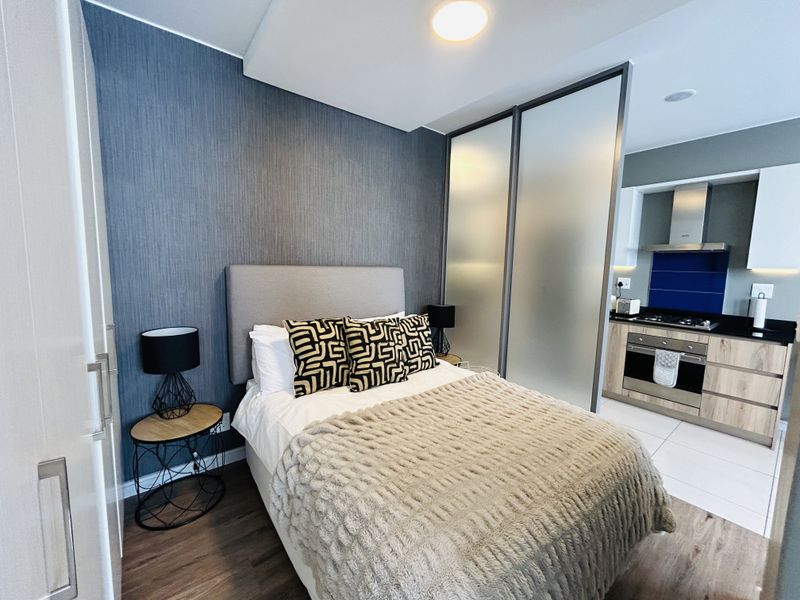 Modern open-plan apartment featuring a bedroom area with a feature wall, separated from a compact, well-equipped kitchen by a stylish frosted glass sliding partition.