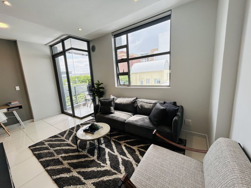 A bright and modern living room featuring large windows, tiled flooring, and direct access to a private balcony.