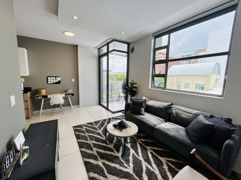 Modern open-plan living area featuring large windows, tiled floors, recessed lighting, and direct access to a private balcony.