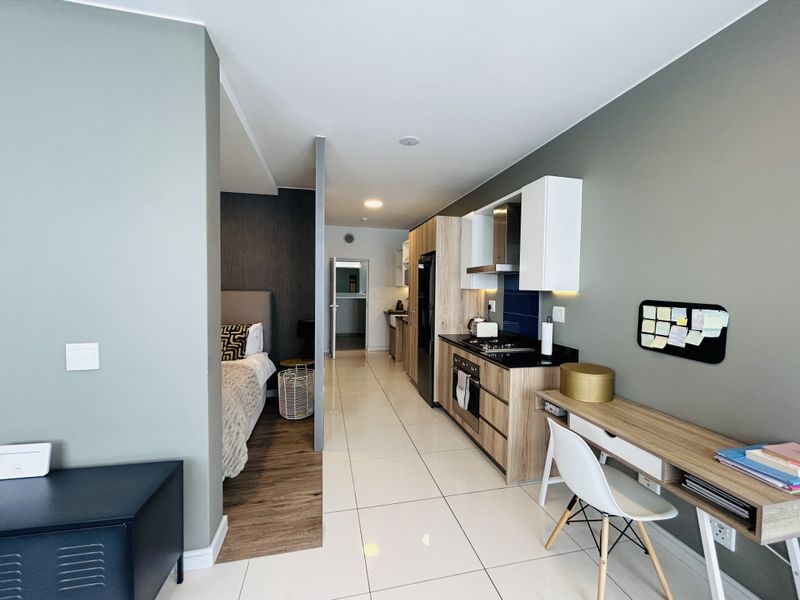 Modern open-plan apartment featuring a sleek kitchen with built-in cabinetry, gas hob, and oven, seamlessly transitioning into a bedroom area with wood-look flooring.