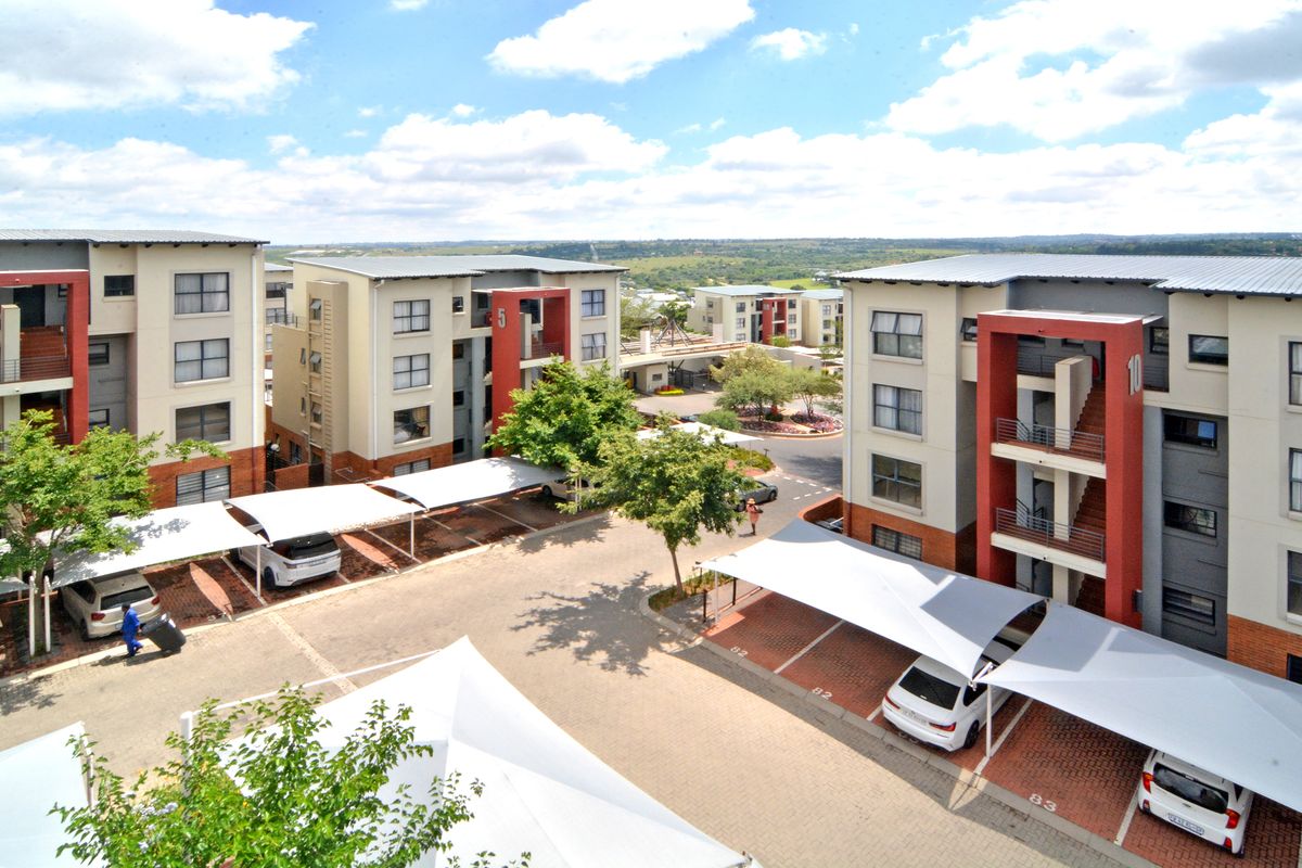 Aerial view of a modern apartment complex featuring multi-story residential buildings, paved driveways, and covered parking bays within a landscaped estate.