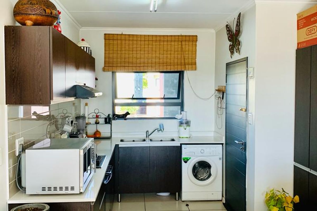 A functional kitchen featuring dark wood cabinetry, a double basin sink, tiled flooring, and a tiled backsplash with integrated appliance space.