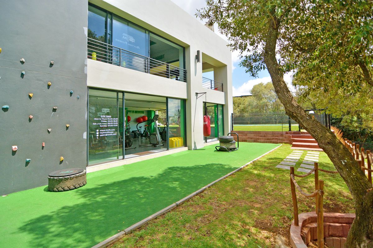 Rear exterior view of a modern apartment building featuring a climbing wall, artificial grass area, and access to a ground-floor gym facility.