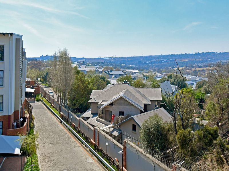 An elevated aerial view showing the apartment complex exterior, paved driveway, and surrounding residential neighbourhood landscape.