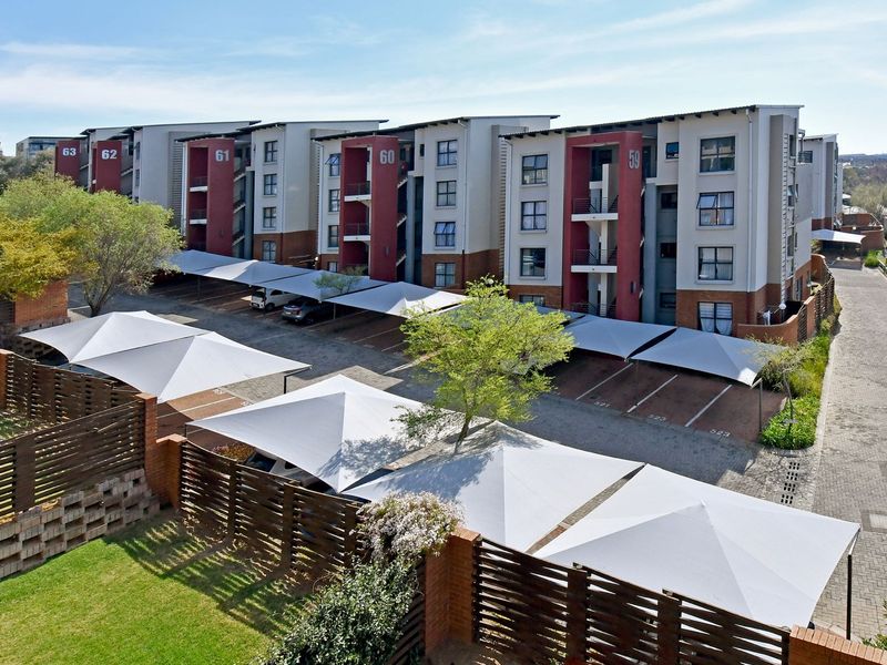 Aerial view of a modern apartment complex featuring multiple residential blocks, paved parking areas with shade cloth carports, and perimeter brick walling.
