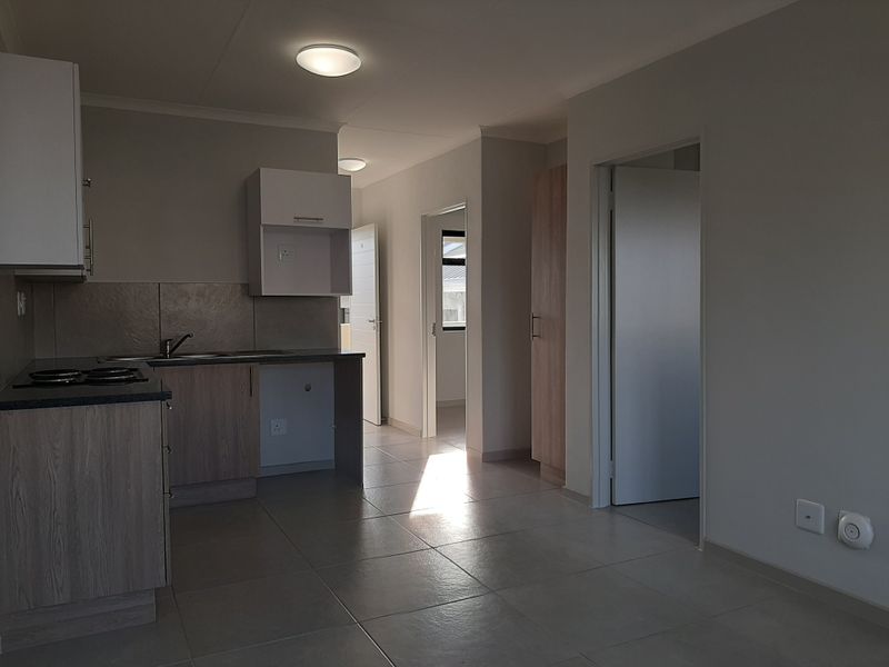 An open-plan kitchen and living area featuring modern cabinetry, tiled flooring, and neutral finishes, providing a clean and functional space.
