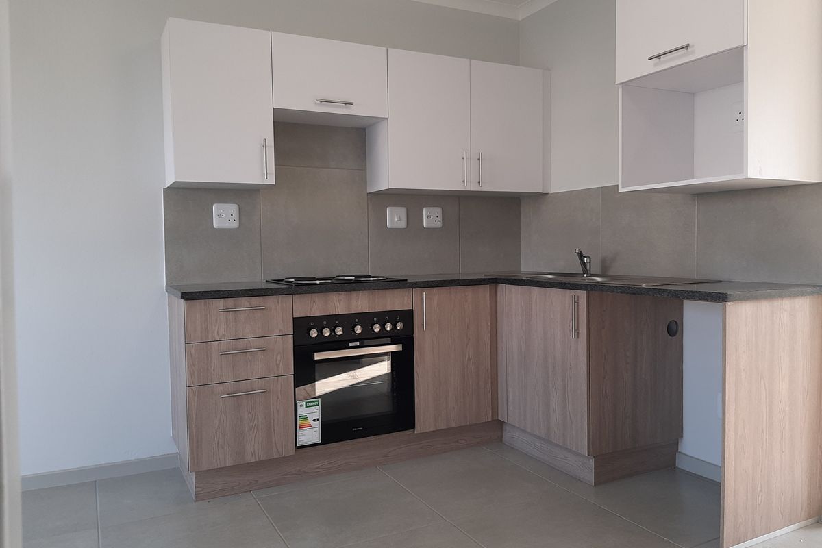 A clean, modern kitchen featuring light wood-finish cabinetry, white upper cabinets, dark countertops, and integrated electric oven and hob with tiled splashbacks.