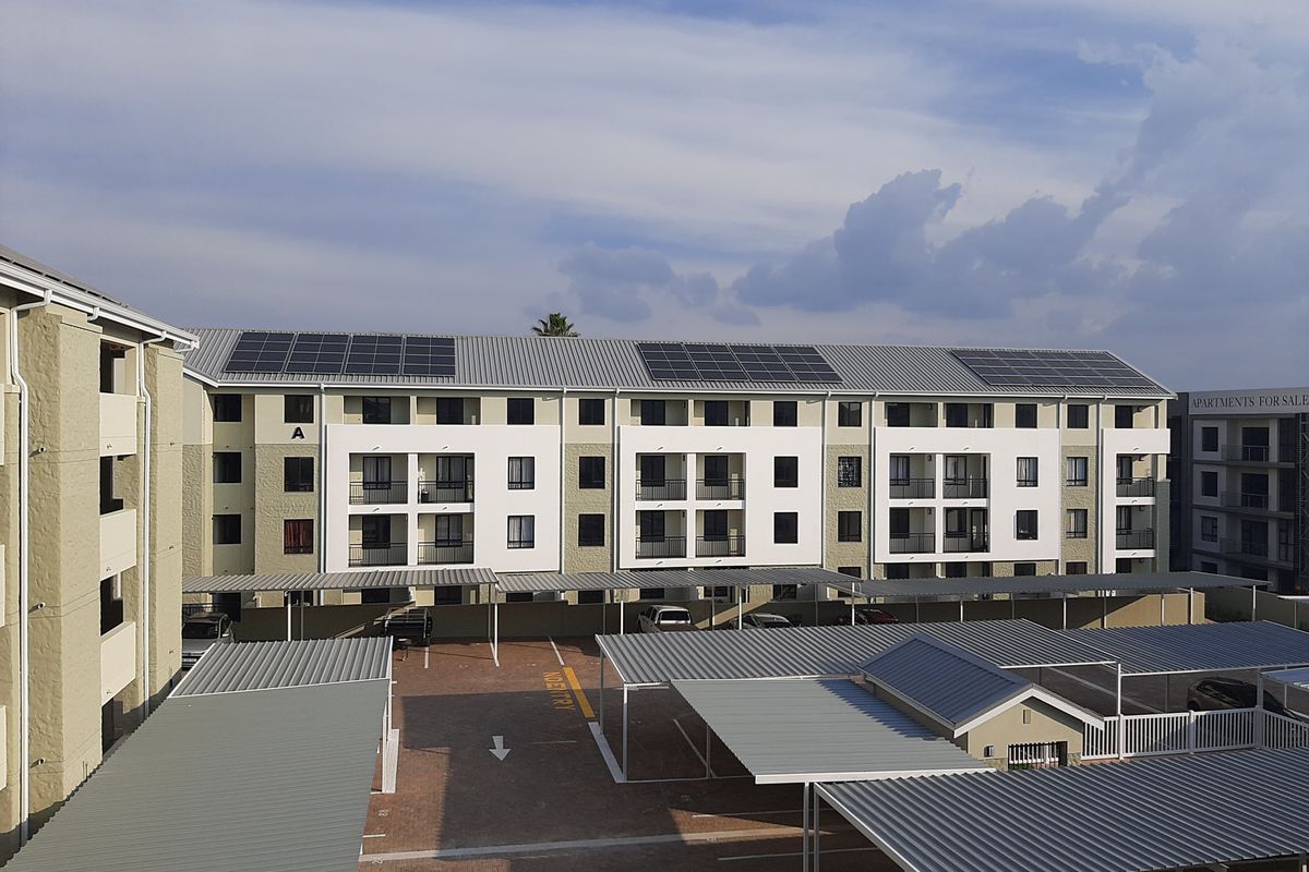 Aerial view of an apartment complex featuring modern architecture, solar panels on the roof, and covered parking bays.