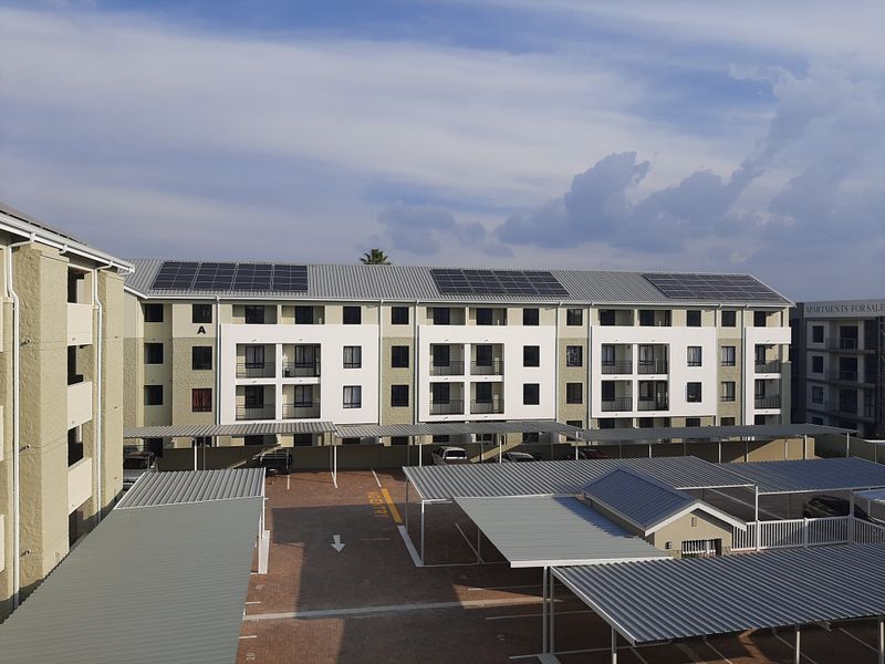 Aerial view of an apartment complex featuring modern architecture, solar panels on the roof, and covered parking bays.