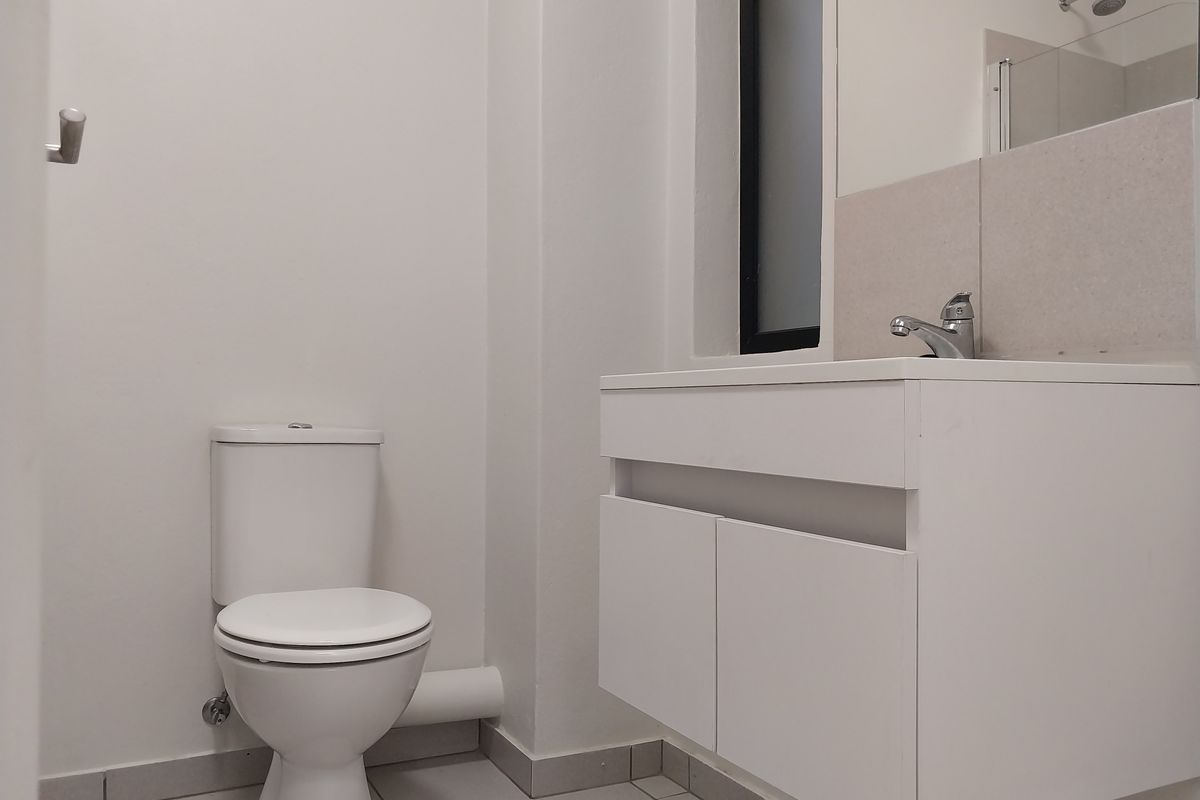 A clean and modern bathroom featuring a white vanity with basin, a toilet, and a shower area with a glass screen.