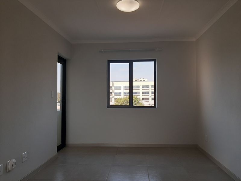 A clean, empty bedroom featuring neutral tiled flooring, modern aluminium window and door frames, and a simple ceiling light fixture.