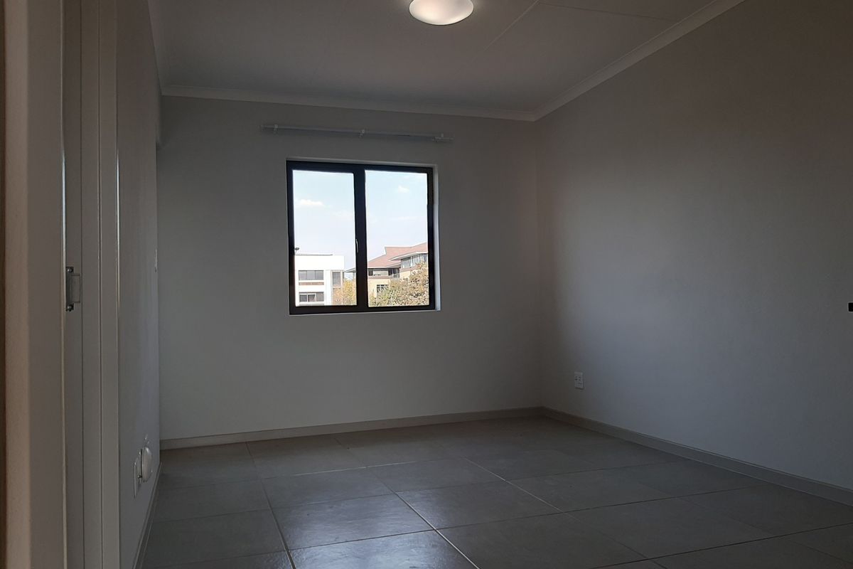 A clean, empty bedroom featuring neutral tiled flooring, a built-in cupboard, and a window providing natural light.