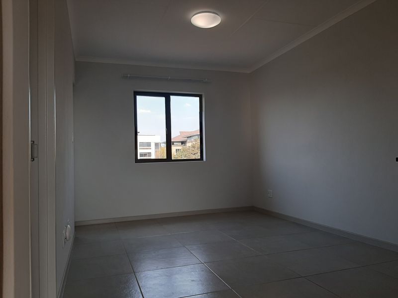 A clean, empty bedroom featuring neutral tiled flooring, a built-in cupboard, and a window providing natural light.