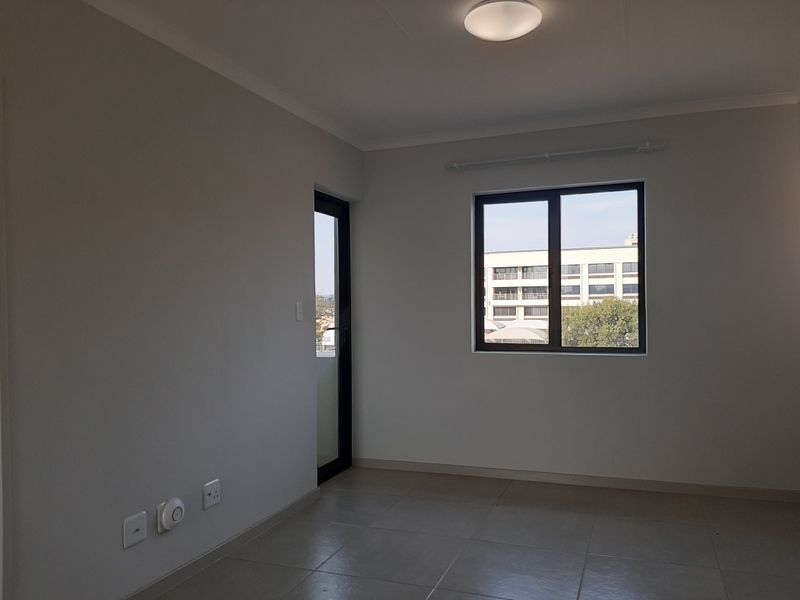 A clean, empty bedroom featuring neutral walls, tiled flooring, and access to an outdoor area through a glass-paneled door.