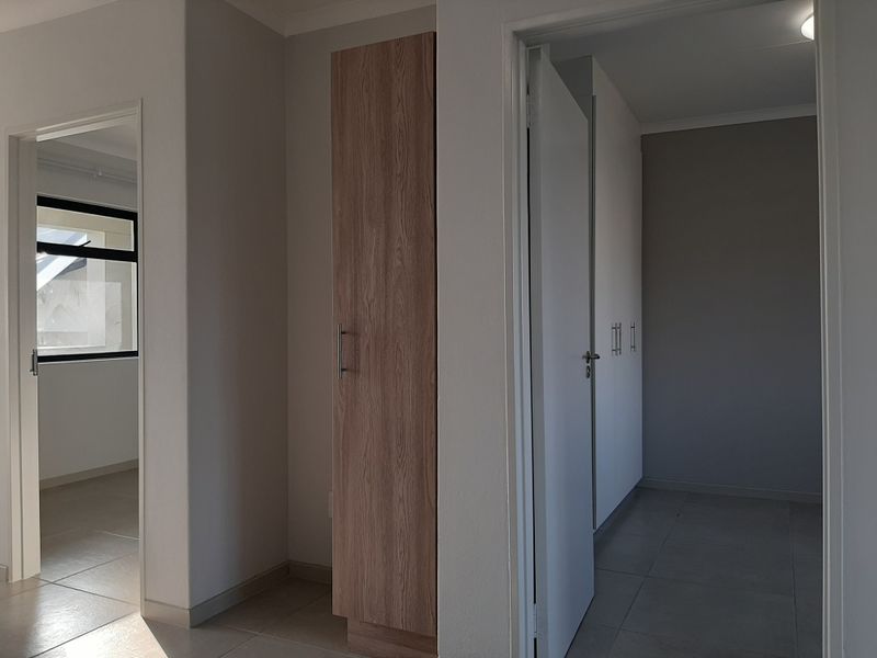 A clean, neutral hallway featuring tiled flooring and built-in wooden cabinetry, providing access to adjacent rooms within the apartment.