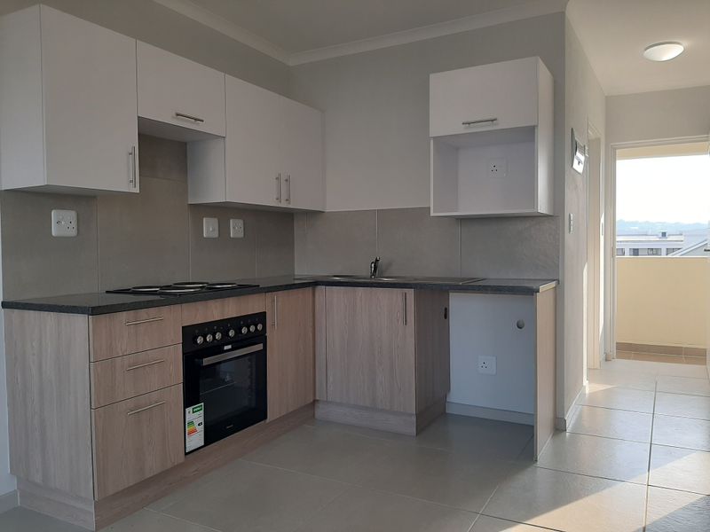 Modern kitchen featuring light wood-tone lower cabinets, white upper cabinetry, dark laminate countertops, built-in oven, electric hob, and tiled flooring.