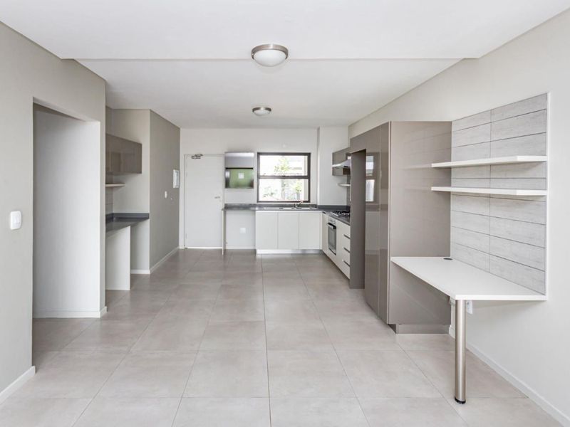 Modern open-plan kitchen and living area featuring sleek cabinetry, integrated appliances, tiled flooring, and a convenient built-in workspace.