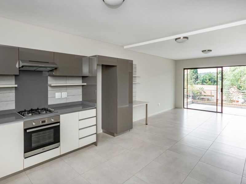Modern open-plan kitchen and living area featuring sleek cabinetry, gas hob, built-in oven, and large sliding doors leading to a private balcony.