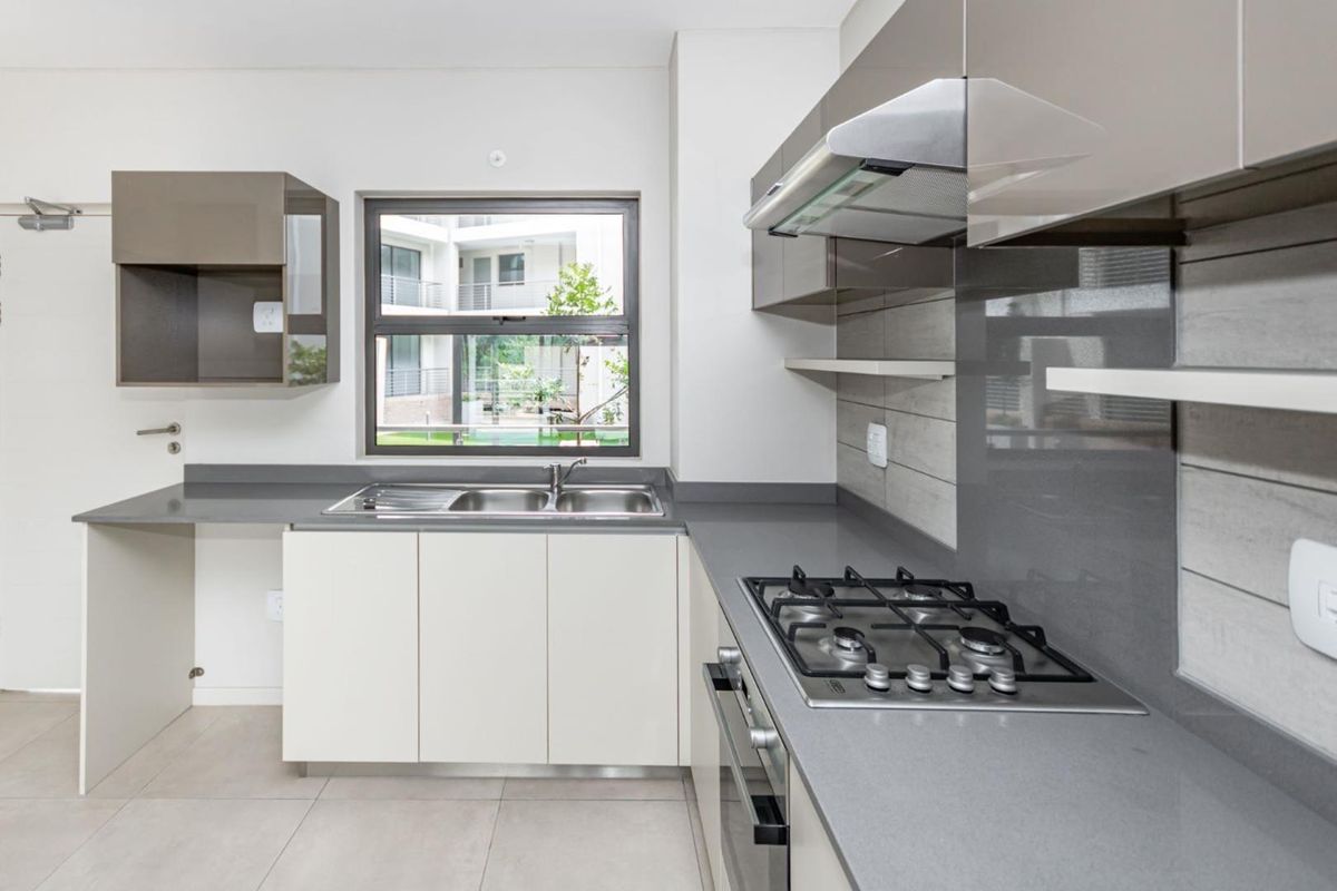 Modern kitchen featuring sleek cabinetry, stone countertops, integrated gas hob, oven, and extractor fan with neutral tiled finishes.