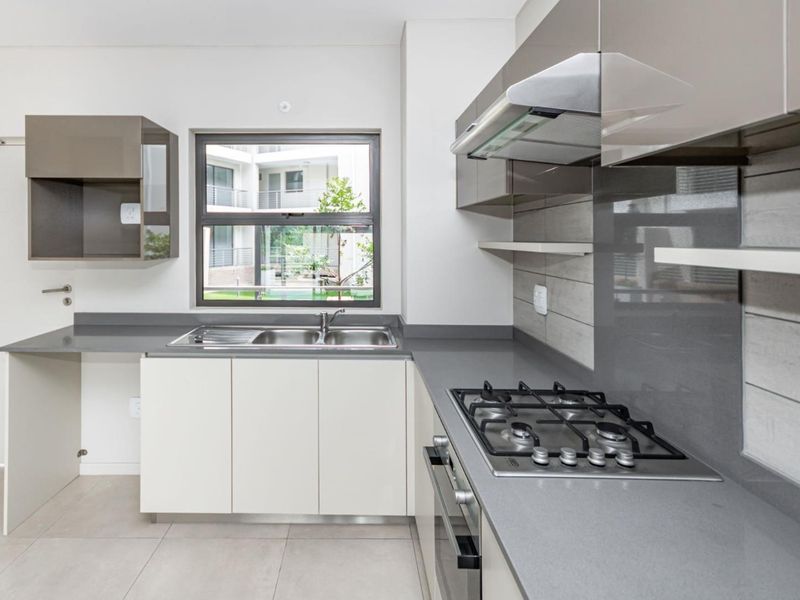 Modern kitchen featuring sleek cabinetry, stone countertops, integrated gas hob, oven, and extractor fan with neutral tiled finishes.