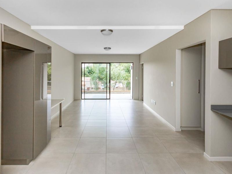 An open-plan living and kitchen area featuring neutral tiled flooring, modern cabinetry, and a sliding glass door leading to an outdoor balcony.