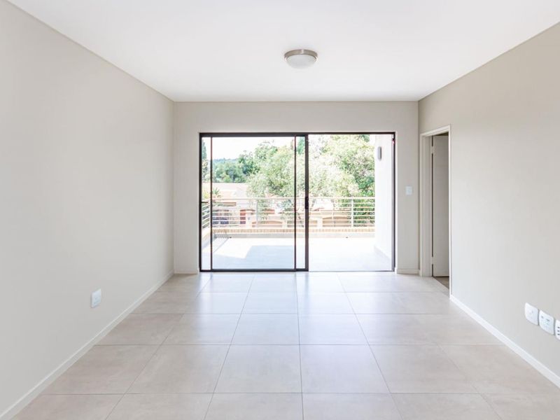A bright, empty living room featuring neutral tiled flooring and a large sliding glass door that opens onto a private balcony.