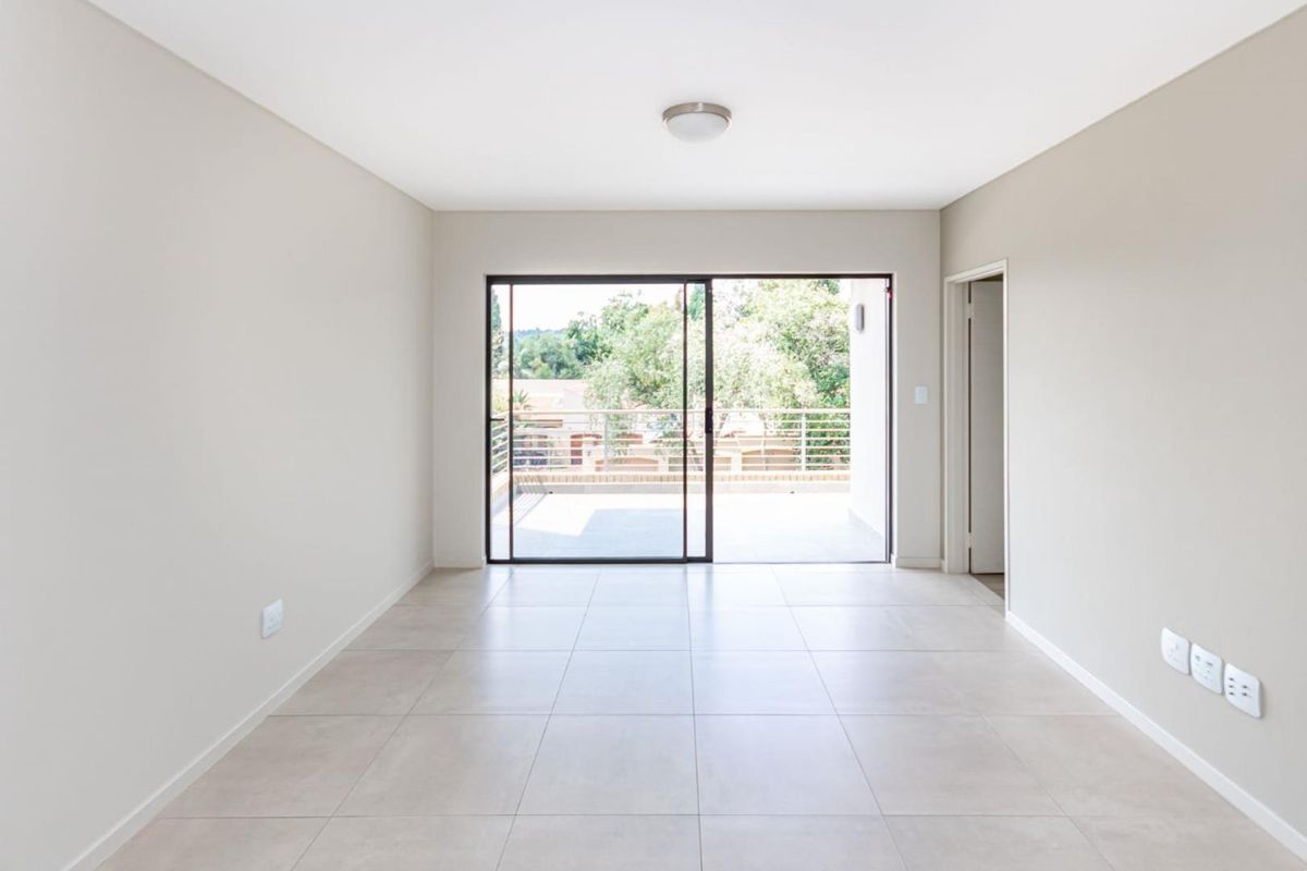 A bright, empty living room featuring neutral tiled flooring and a large sliding glass door that opens onto a private balcony.