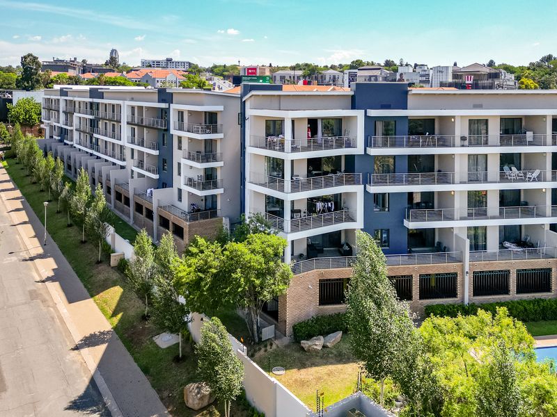 Aerial view of a modern multi-story apartment complex featuring private balconies, landscaped grounds, and a swimming pool in a well-maintained residential setting.