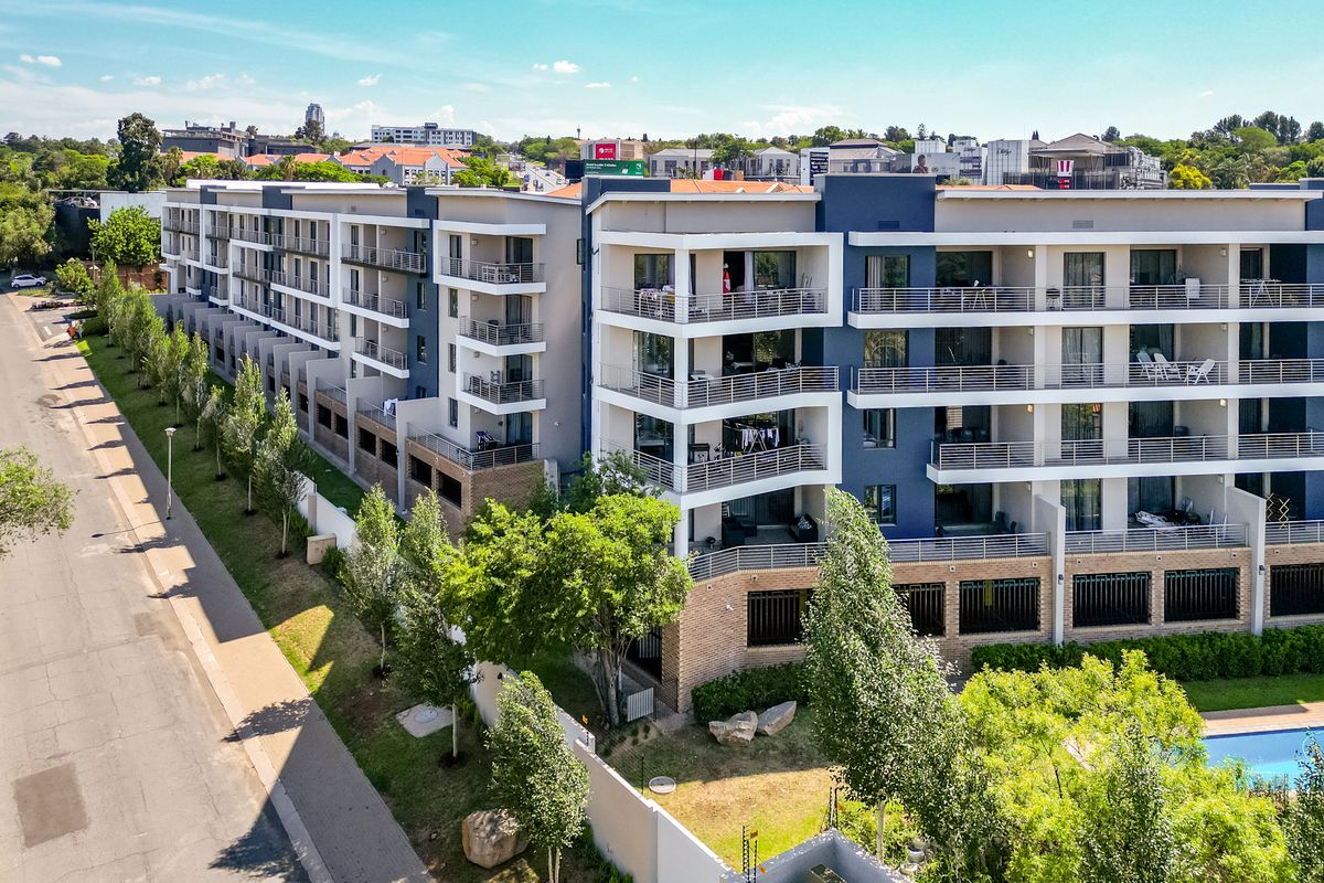 Aerial view of a modern multi-story apartment complex featuring private balconies, landscaped grounds, and a swimming pool in a well-maintained residential setting.
