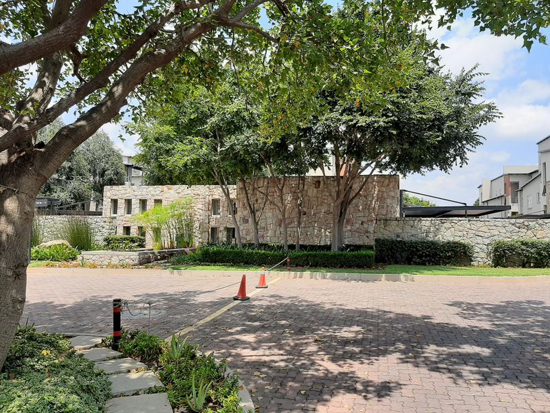 Front entrance view of the apartment complex featuring stone-clad boundary walls, mature trees, and a paved driveway.