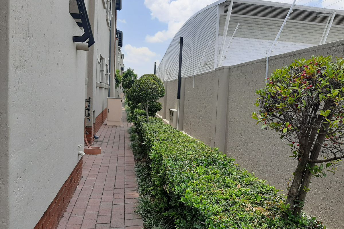 A side walkway featuring paved flooring, a well-maintained hedge, and a secure boundary wall with electric fencing.