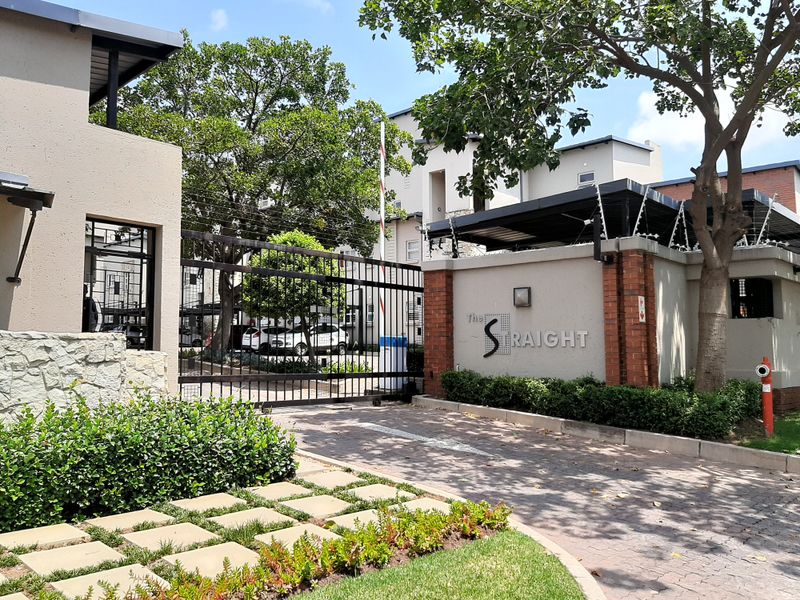 The secure entrance to The Straight apartment complex, featuring a gated access point, electric fencing, and well-maintained brick boundary walls and landscaping.