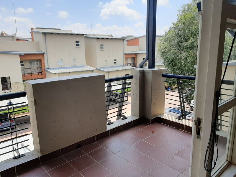 A private balcony featuring tiled flooring, a metal balustrade, and a concrete parapet wall, overlooking the apartment complex grounds.