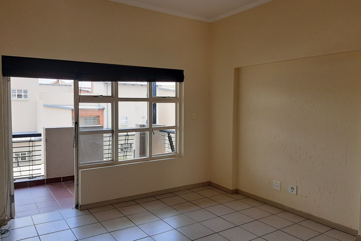 An empty living room featuring tiled flooring, neutral walls, and a sliding glass door providing access to a private balcony.