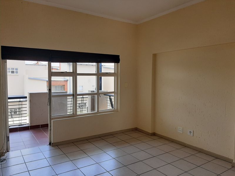 An empty living room featuring tiled flooring, neutral walls, and a sliding glass door providing access to a private balcony.