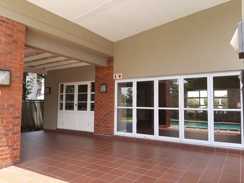 A spacious covered patio featuring tiled flooring, exposed brick accents, and large folding glass doors that provide seamless access to the outdoor pool area.