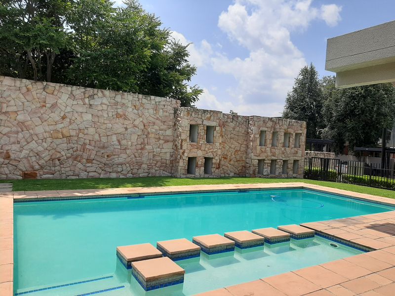 A well-maintained swimming pool area featuring a decorative stone boundary wall and integrated tiled steps, set within a landscaped garden environment.