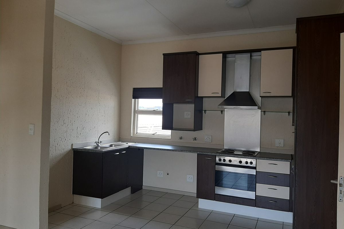 A functional kitchen featuring dark and light cabinetry, built-in oven and hob, stainless steel extractor fan, and tiled flooring.