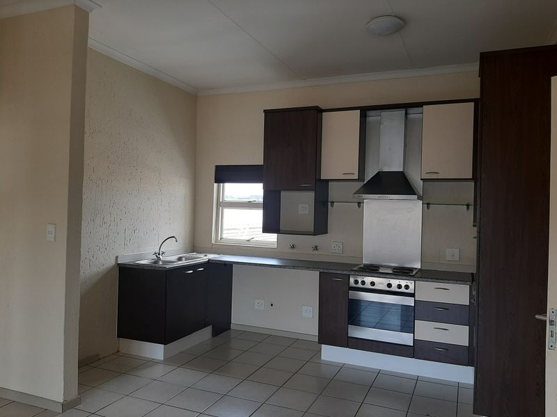 A functional kitchen featuring dark and light cabinetry, built-in oven and hob, stainless steel extractor fan, and tiled flooring.